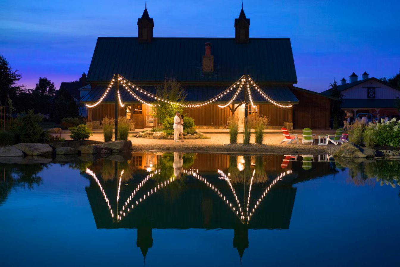 Lantern-lit event barn reflected in a pond at dusk